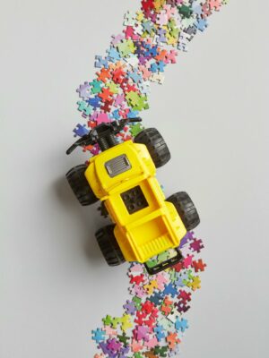 A colorful toy truck driving through scattered puzzle pieces on a light background.