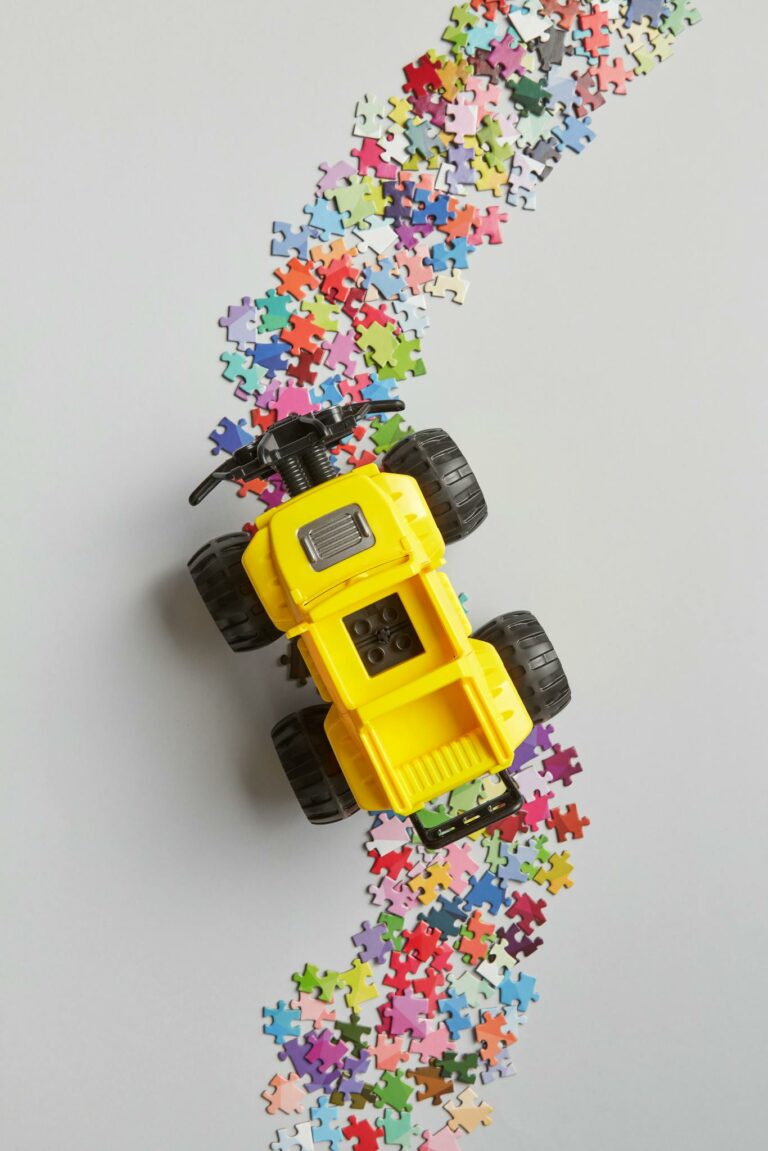 A colorful toy truck driving through scattered puzzle pieces on a light background.