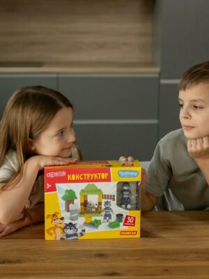 Two children interacting with a building block toy set indoors, fostering creativity and play.