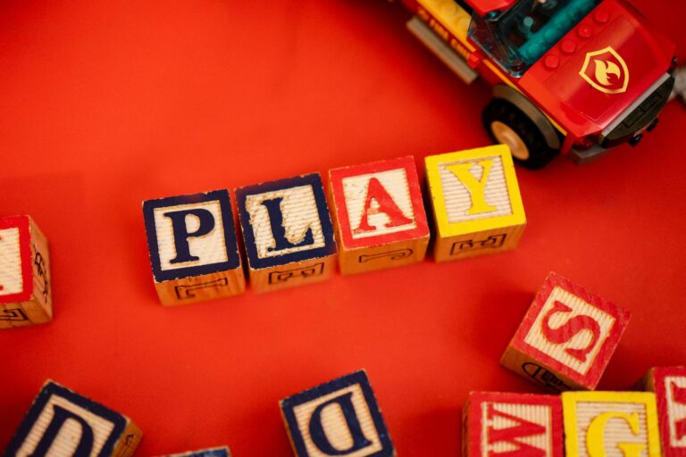 Wooden alphabet blocks spelling 'PLAY' beside a toy car on a red background.